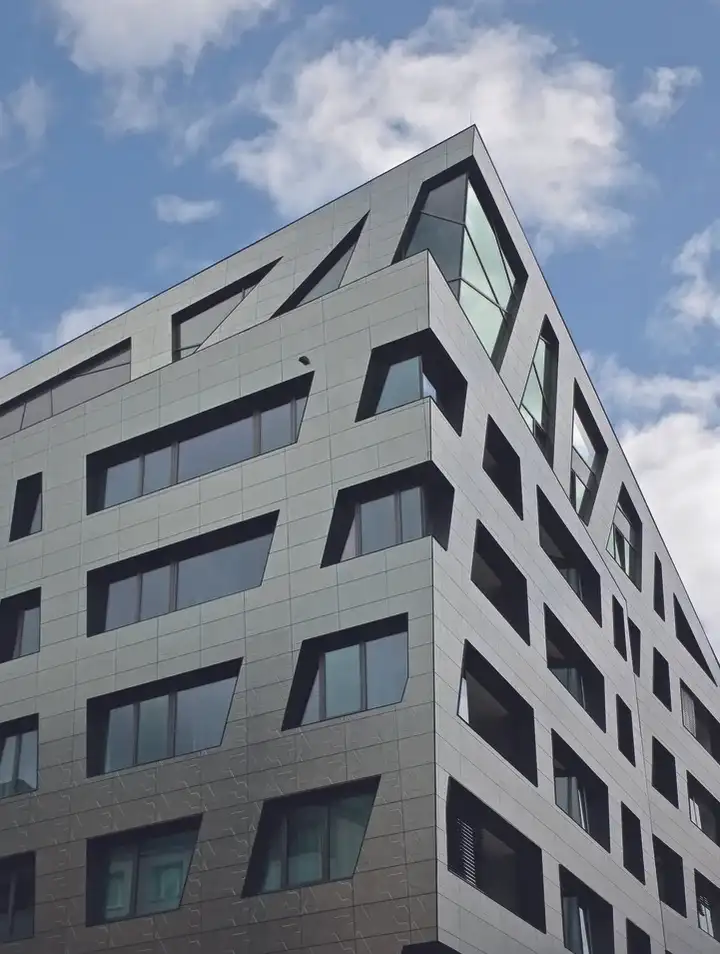 Edificio de oficinas con fachada de placas BioStone20 SNS® grises bajo un cielo con nubes