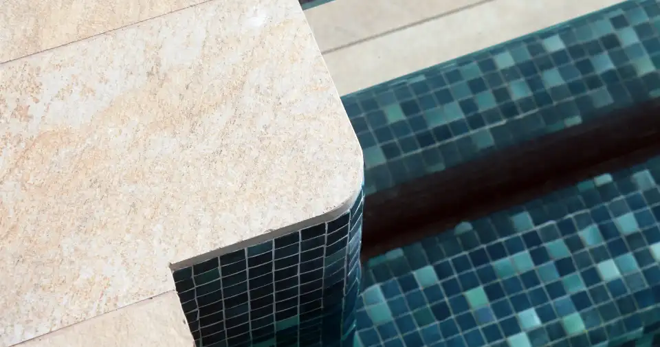 Borde de piscina con pavimento de piedra clara y gresite azul
