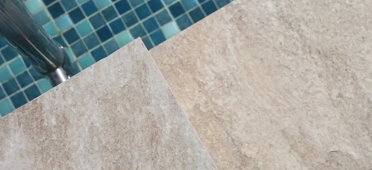 Pavimento de piedra clara en el borde de una piscina con gresite azul